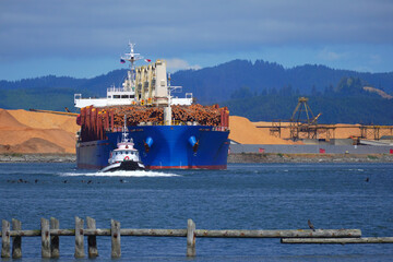 Tug boat leading a bulk carrier loaded with timber