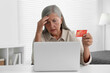 © New Africa - Upset woman with credit card near laptop at table indoors. Be careful - fraud