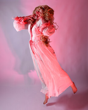 Full length portrait scary vampire zombie bride wearing bloody halloween fantasy costume dress. Dynamic jumping pose gestural arms reaching out. Isolated  studio backdrop with cinematic red lighting.