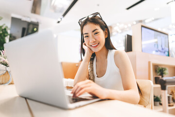 Wall Mural - Young asian woman sitting indoors cafe using laptop influencer gen z modern lifestyles