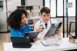 © Nuttapong punna - Focused mature male doctor and African female nurse look at tablet and laptop discuss anamnesis together. Concentrated diverse medical professionals in hospital.