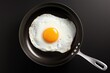 One fried egg in hot pan on black background, top view