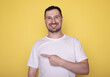 © lashkhidzetim - Handsome young man point by finger right side with happy face looking at camera on yellow isolated background.