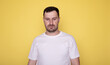 © lashkhidzetim - Portrait of serious sad upset man with beard wearing white T-shirt standing looking at camera, expressing sorrow and sadness, hearing bad news. Indoor studio shot isolated on yellow background.
