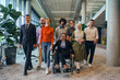 In a spacious and modern startup office, a diverse group of business colleagues, including a colleague in a wheelchair, collaborates and interacts, exemplifying inclusivity, diversity, and teamwork in