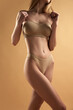 © Lustre Art Group  - Cropped photo of young slim beautiful girl wearing beige color underwear posing over brown background. Concept of beauty, body care, healthy eating