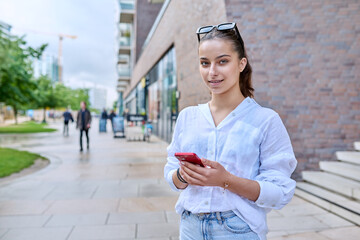 Portrait of young teenage female with smartphone, on street of modern city