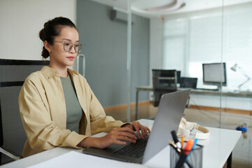 Young female software developer working on laptop at office desk