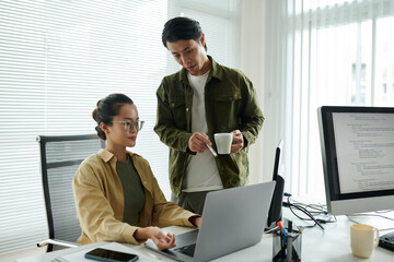 senior software developer helping junior colleague to fix bugs in programming code