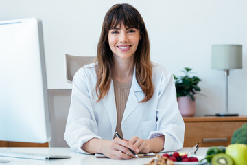 Beautiful smart nutritionist woman working with computer while looking at camera in the nutritionist consultation