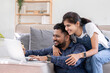 © wichayada - Cropped view of young woman hugging husband while using laptop on sofa in living room