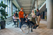 © .shock - A diverse group of business colleagues is having fun with their wheelchair-using colleague, demonstrating their attention and inclusivity in the workplace