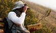 Book, binocular or man bird watching in nature on trekking adventure journey for wellness or peace. Hiking, holiday vacation or African person on bench to relax or looking to search in park for view