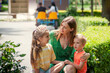 © Марина Лола - Mother and two children are sitting on park bench. Mother talks to her daughter and hugs children. Parents and children, upbringing, mutual understanding, emotional intelligence, emotional closeness