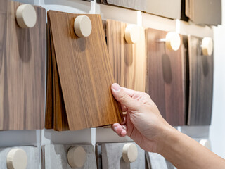 Wall Mural - designer hand picking wood samples board from material swatch wall display in material library. choo