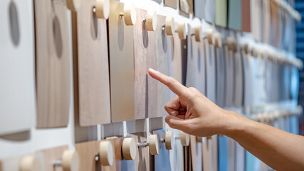 Wall Mural - Designer hand pointing wood samples board on material swatch wall display in library. Choosing wooden laminate texture in brown and beige tone collection for interior architecture or furniture design