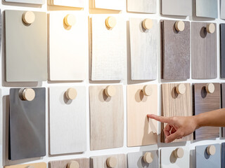 Wall Mural - Designer hand pointing wood samples board on material swatch wall display in library. Choosing wooden laminate texture in brown and beige tone collection for interior architecture or furniture design