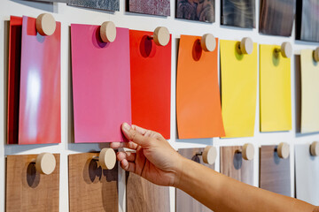 Wall Mural - Designer hand picking colorful laminate sheet on material swatch wall display in material library. Choosing color board from collection for interior architecture and furniture finishing design