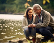 A White grandpa and his Latinx, mixed-ethnicity granddaughter share smiles and fishing lessons by the river. Ideal for themes of family bonding, diversity, and outdoor learning.