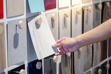 Wall Mural - Designer hand picking wood samples board from material swatch wall display in material library. Choosing wooden laminate texture in gray tone collection for interior architecture or furniture design