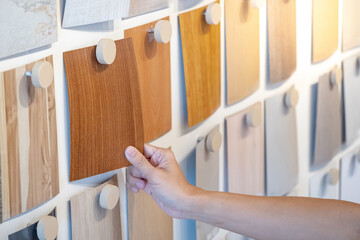 Wall Mural - Designer hand picking wood samples board from material swatch wall display in material library. Choosing wooden laminate texture in brown tone collection for interior architecture or furniture design