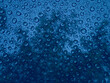 Las gotas de lluvia sobre un cristal color azul en el vidrio de la  ventana de la casa, con sombra de las hojas de los árboles en silueta, forma un diseño abstracto muy original para los fondos