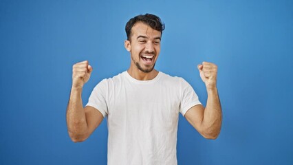 Wall Mural - Young hispanic man smiling confident standing with winner gesture over isolated blue background