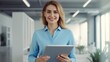 © WS Studio 1985 - CEO of a company is standing in her office, holding a digital tablet with a fintech tab application.