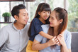 © aekkorn - Portrait of a happy young family. Mom, dad and daughter look at the camera and smile sitting on sofa in living room. The faces of Asian parents and their child.