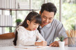 © aekkorn - Children education and home school concept : Young asisn father pleased to see little daughters' study success. Excited smiling small child girl enjoying learning and writing with pleasant dad at home