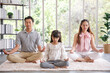© aekkorn - Young  asian family with daughter sit on floor practice yoga together, happy parents with girl child rest on floor meditate relieve negative emotions on weekend at home.