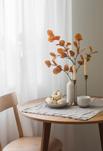 Autumn Home Interior In The Living Room - Around Wooden Table, A Chair, A Bouquet Of Autumn Leaves In A Vase, Decorative Pumpkins. Cozy Home