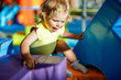 © Irina Schmidt - Happy blond little toddler girl having fun and sliding on indoor playground at daycare or nursery. Positive funny baby child smiling. Healthy girl climbing on slide.