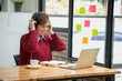© PHAISITSAWAN - Beautiful Asian businesswoman sitting at a table with computer wearing headphones with microphone Looking at the laptop camera Happy businesswoman educating customers online.