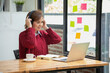 © PHAISITSAWAN - Beautiful Asian businesswoman sitting at a table with computer wearing headphones with microphone Looking at the laptop camera Happy businesswoman educating customers online.