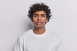 Portrait of handsome curly haired Hindu man concentrated at camera with attentive gaze poses for making photo on documents wears white clothing stands in studio. Serious boyfriend listens explanations
