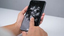 Female hand holding a smartphone with a broken screen and touching the screen isolated on white background. Smartphone damage, touch screen scratched with spider web.