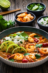 Wall Mural - Tom Yum soup - Thai soup with prawns and rice noodles on wooden table

