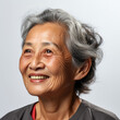 Professional studio head shot of a joyful 70-year-old Southeast Asian woman, eyes looking down.
