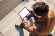 © baranq - Mockup of man in coat sitting on stairs using digital tablet with white blank screen