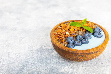 Bowl of granola with yogurt and fresh berries on a texture table. Yogurt berries, acai bowl, spirulina bowl. Healthy food, balanced breakfast. Strawberries, blueberries, kiwi, peach, almonds and chia.