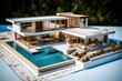 A modern architectural model of a house with a pool sitting on blueprints, made of white and wood materials.