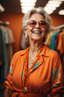 © kapros76 - Happy senior woman in colorful orange outfit, cool sunglasses, laughing and having fun in fashion studio. Image created using artificial intelligence.