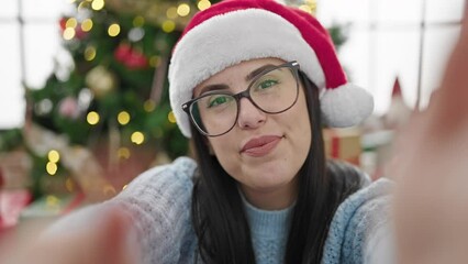 Canvas Print - Young hispanic woman waving to the camera by christmas tree doing video call at home