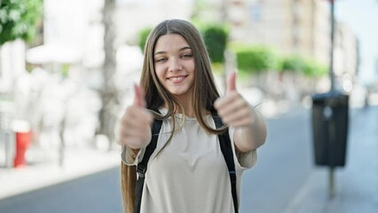 Poster - Young beautiful girl student wearing backpack doing thumbs up gesture at street