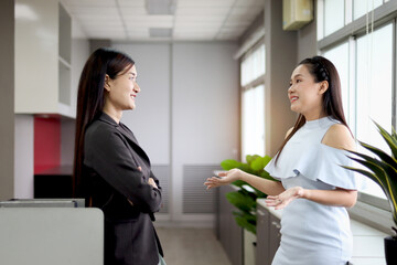 two happy beautiful asian women officers standing and talking during take break from work at office 