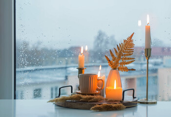 Poster - autumn still life with burning candles and a cup of coffee on the background of a window with raindrops