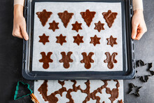 culinary, cooking and christmas concept - close up of hands holding baking tray with cookies made of gingerbread dough on black kitchen table top