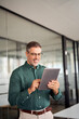 © insta_photos - Smiling busy middle aged business man investor using tablet computer, mature older businessman executive manager looking at tab satisfied with finance trading market standing in office. Vertical