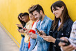 © Xavier Lorenzo - Happy group of young multiracial friends using their smartphones together outside. Gen z people addicted to social media app, watching and sharing content on mobile phone over yellow background.